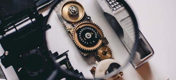 A person using magnifying glass to see gold and white device gear of a camera parts (1)