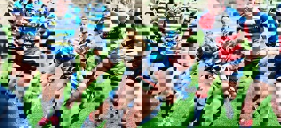 Rugby game with one of the players holding a ball and the other tackling that player from behind.