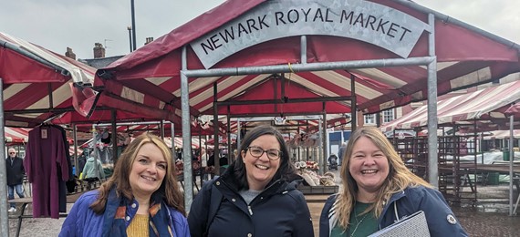 Three people standing in front of town market. They are smiling into the camera.