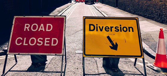 Two signs: one red saying "road closed", one yellow saying "diversion" on a closed road.