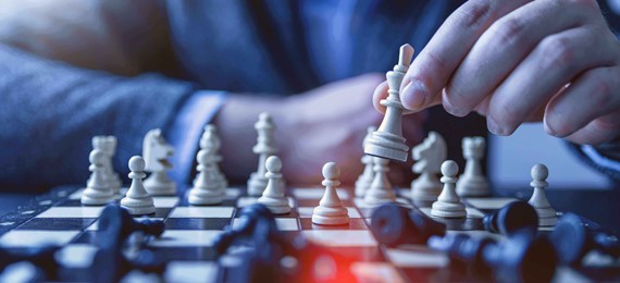 A chess board with a hand of a person holding one of chess pieces.