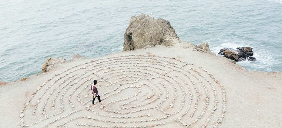 A person walking in a labyrinth made out of stones laid out on a beach.