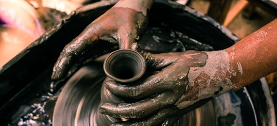 Two hands shaping a clay vase on a potter's wheel.