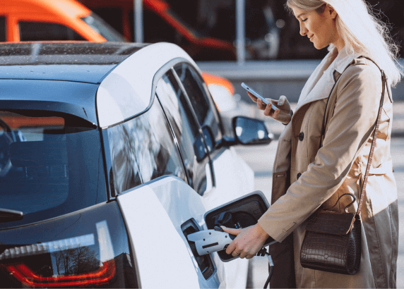 A person plugging charger into an electric vehicle while looking at the cellphone.