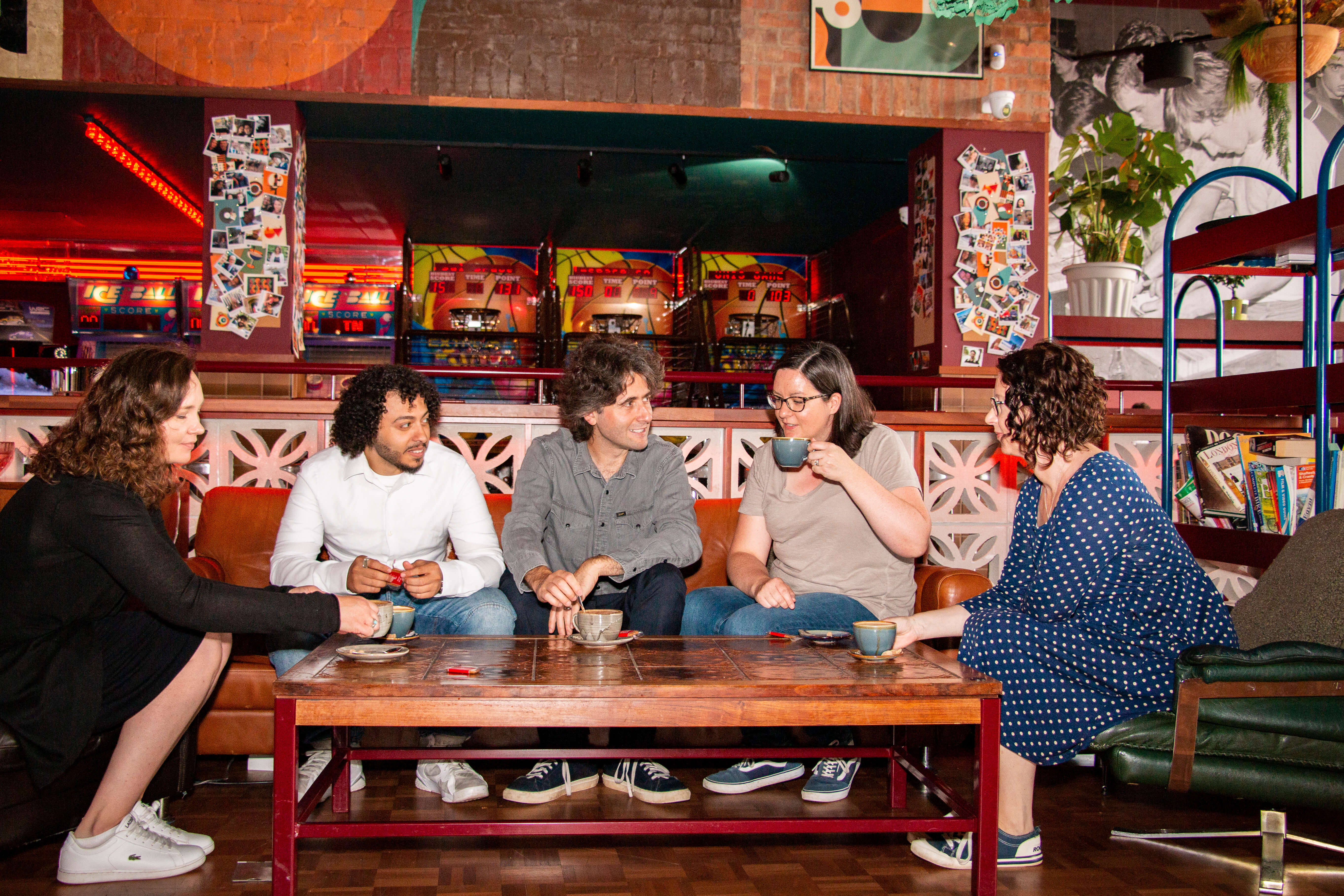 Five people sitting in a cafe talking and drinking coffee.