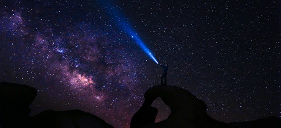 Person shining light at the night sky full of stars